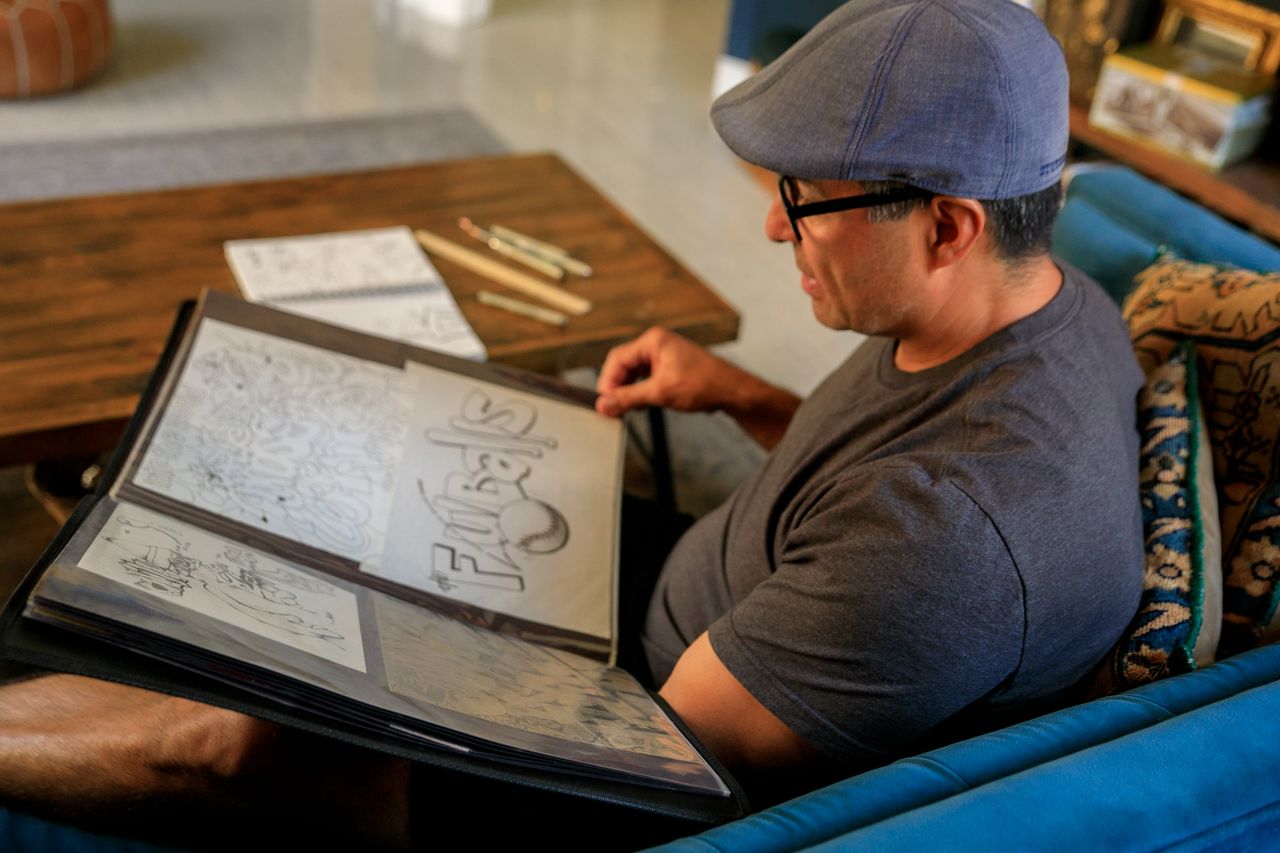 Crafting Captivating Headlines: Your awesome post title goes here A man sits on a sofa reviewing his art portfolio filled with various illustrations.