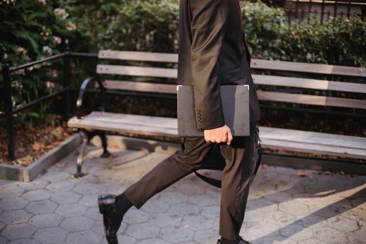 services-04 An anonymous man in a black suit walks in a park holding a portfolio, showcasing a professional urban lifestyle.