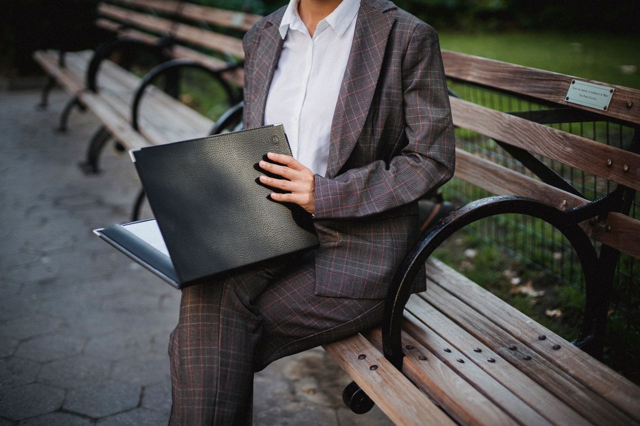 services-01 Businesswoman with a folder sitting on a wooden bench, wearing a checkered suit and white shirt.