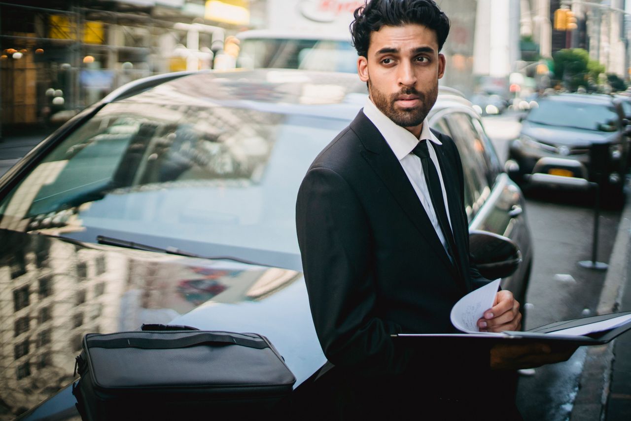 services-02 Stylish businessman in a suit leans on a car in a bustling city street.