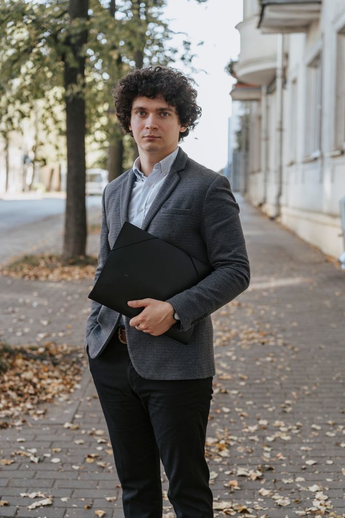 about-us A business professional in a suit holding a document outdoors on a leaf-lined pathway.